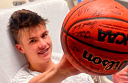 Un joven en una cama de hospital sostiene feliz una pelota de baloncesto autografiada.