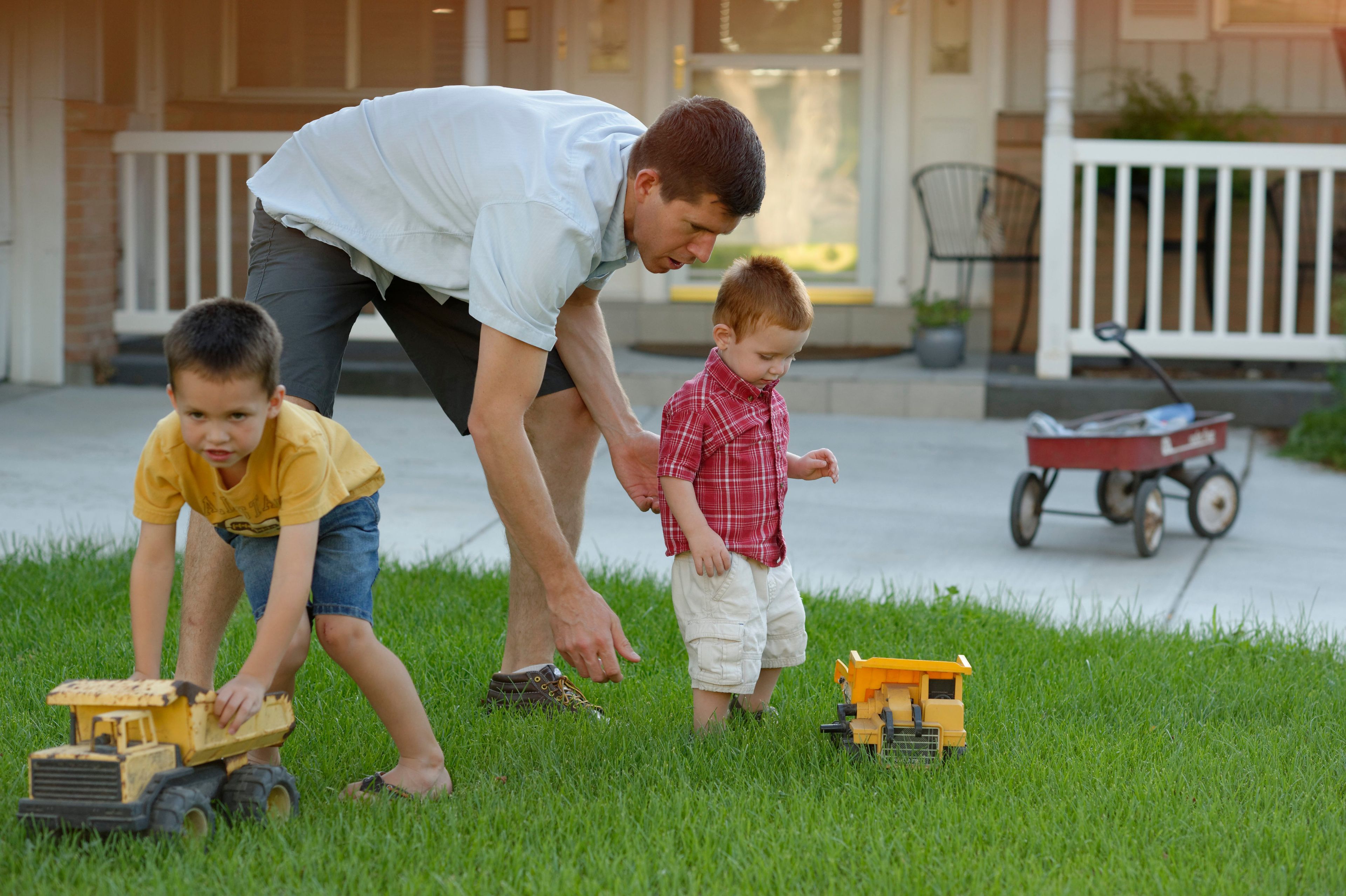 A father plays with his two sons outside in their yard.