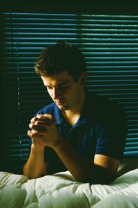 A young man kneeling in prayer at his bedside.