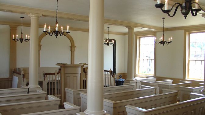 Interior room with pulpit and pews with sunlight streaming through windows.