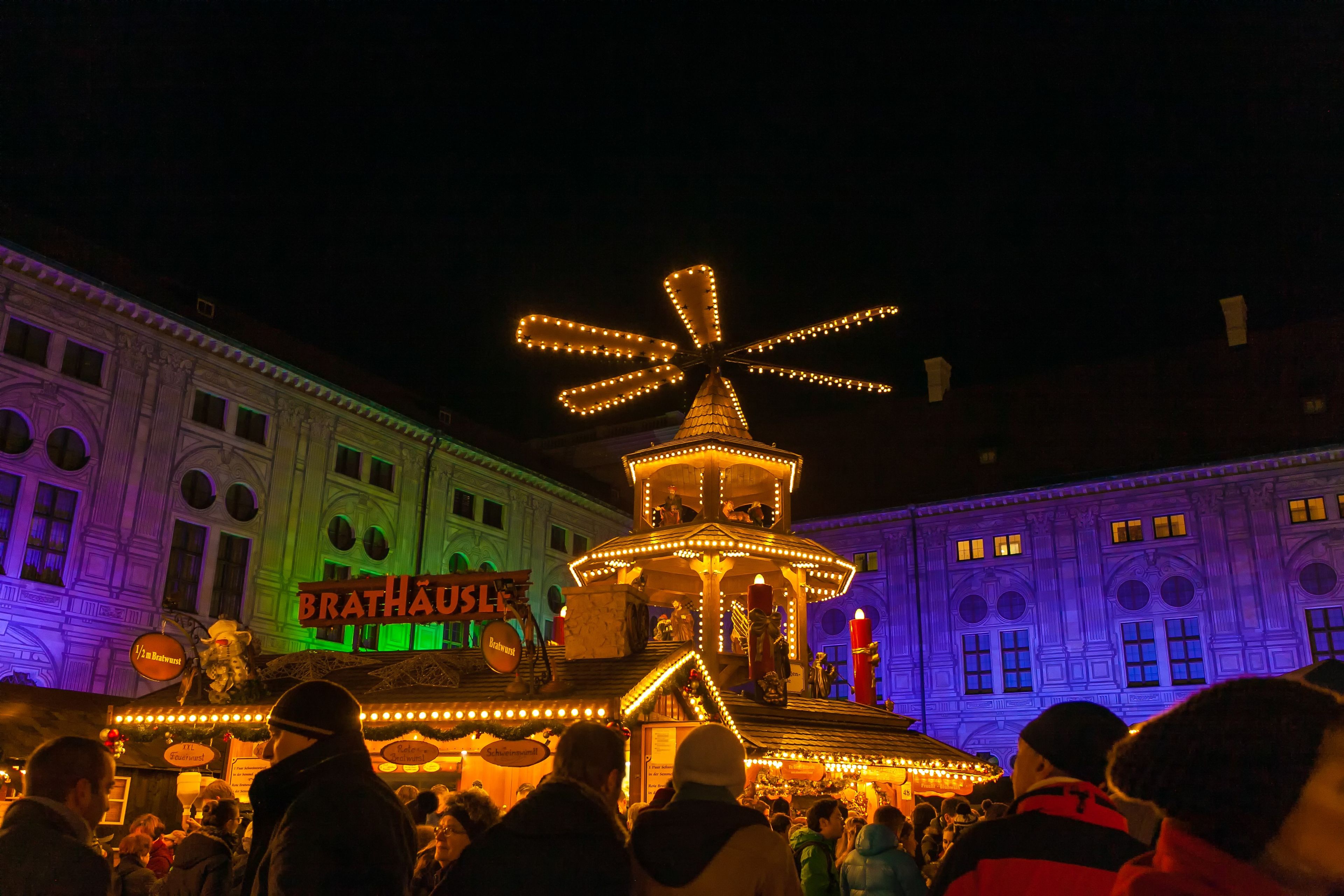 A large, illuminated Christmas pyramid overlooks a bustling Christmas market at night.
