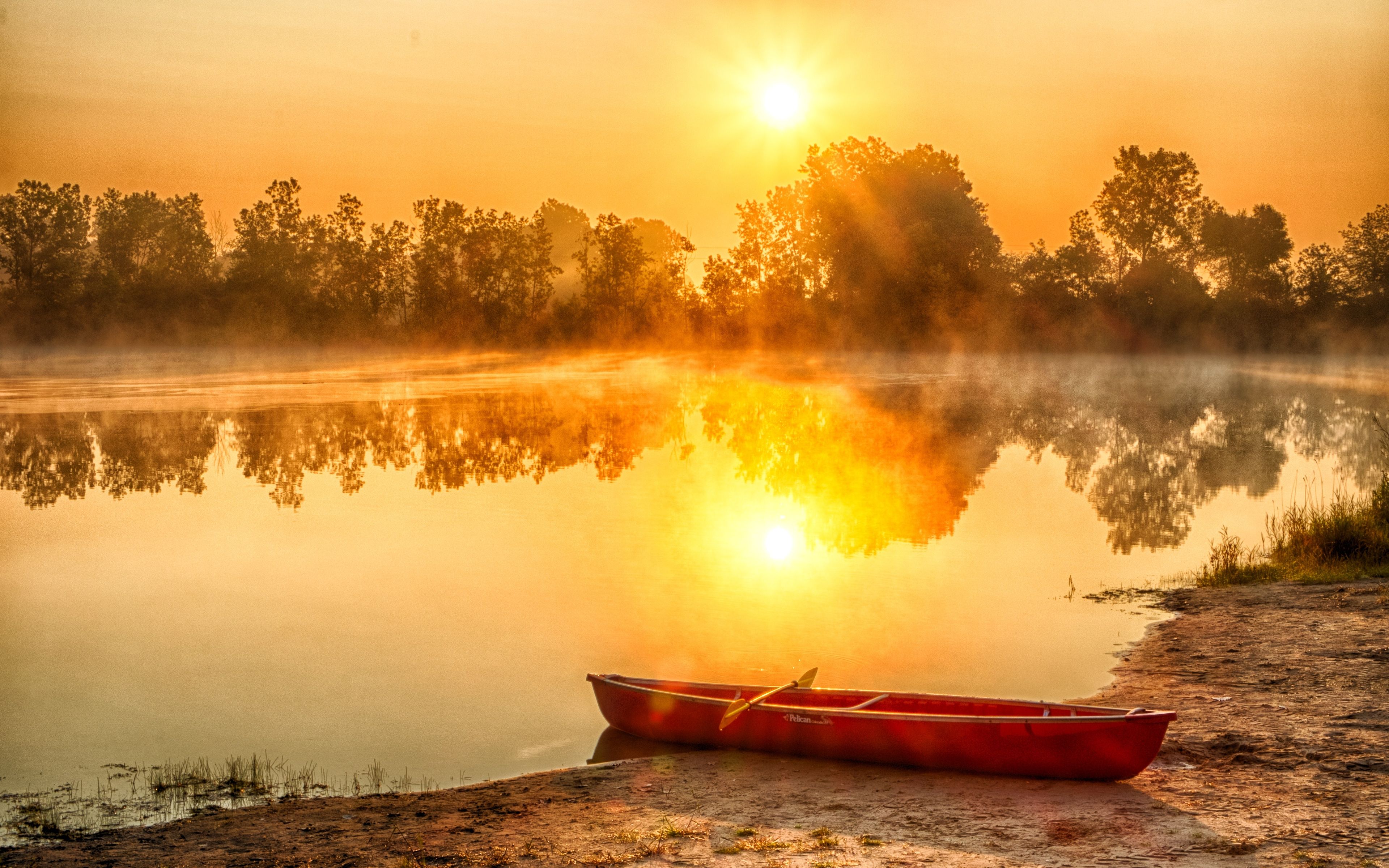 A canoe docked on the edge of a lake with the sun reflected in the water.