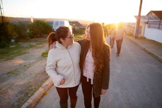 Wanita dan gadis berjalan bersama, saling berangkulan.