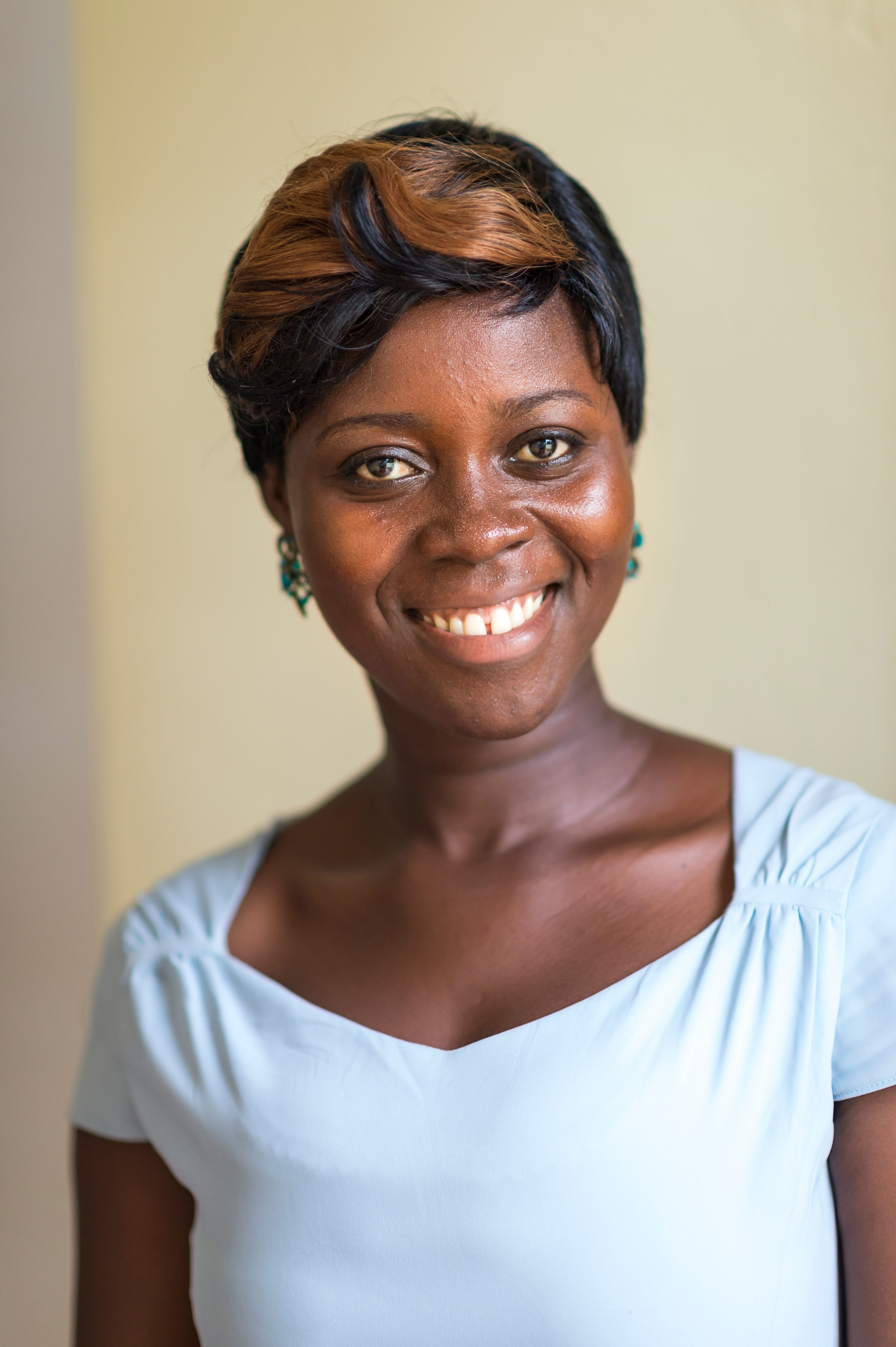A portrait of a young woman in Africa, wearing a blue blouse, smiling.