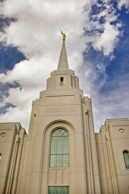 A view of the Brigham City Utah Temple spire as seen from below, with a blue sky and large white clouds.