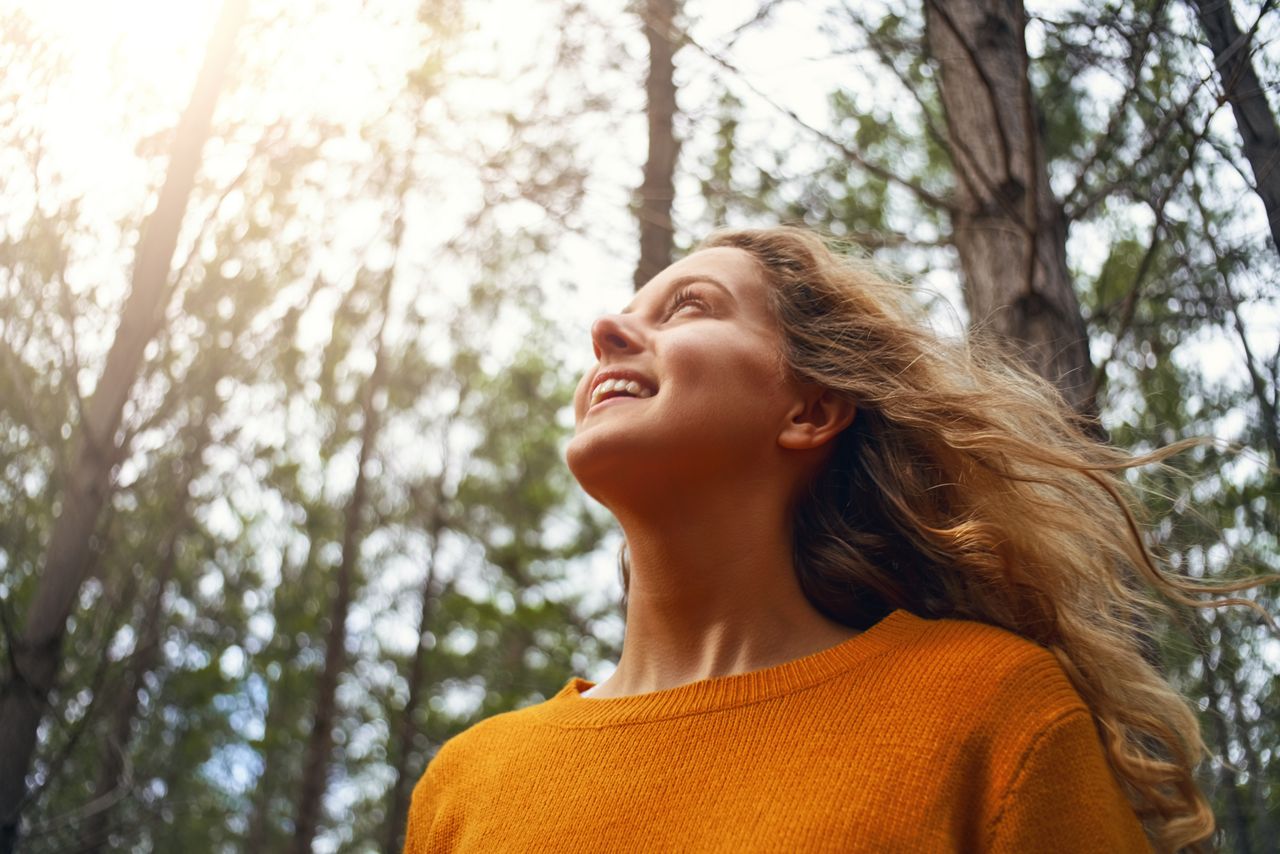 Uma moça sorri apreciando a luz do sol em uma floresta
