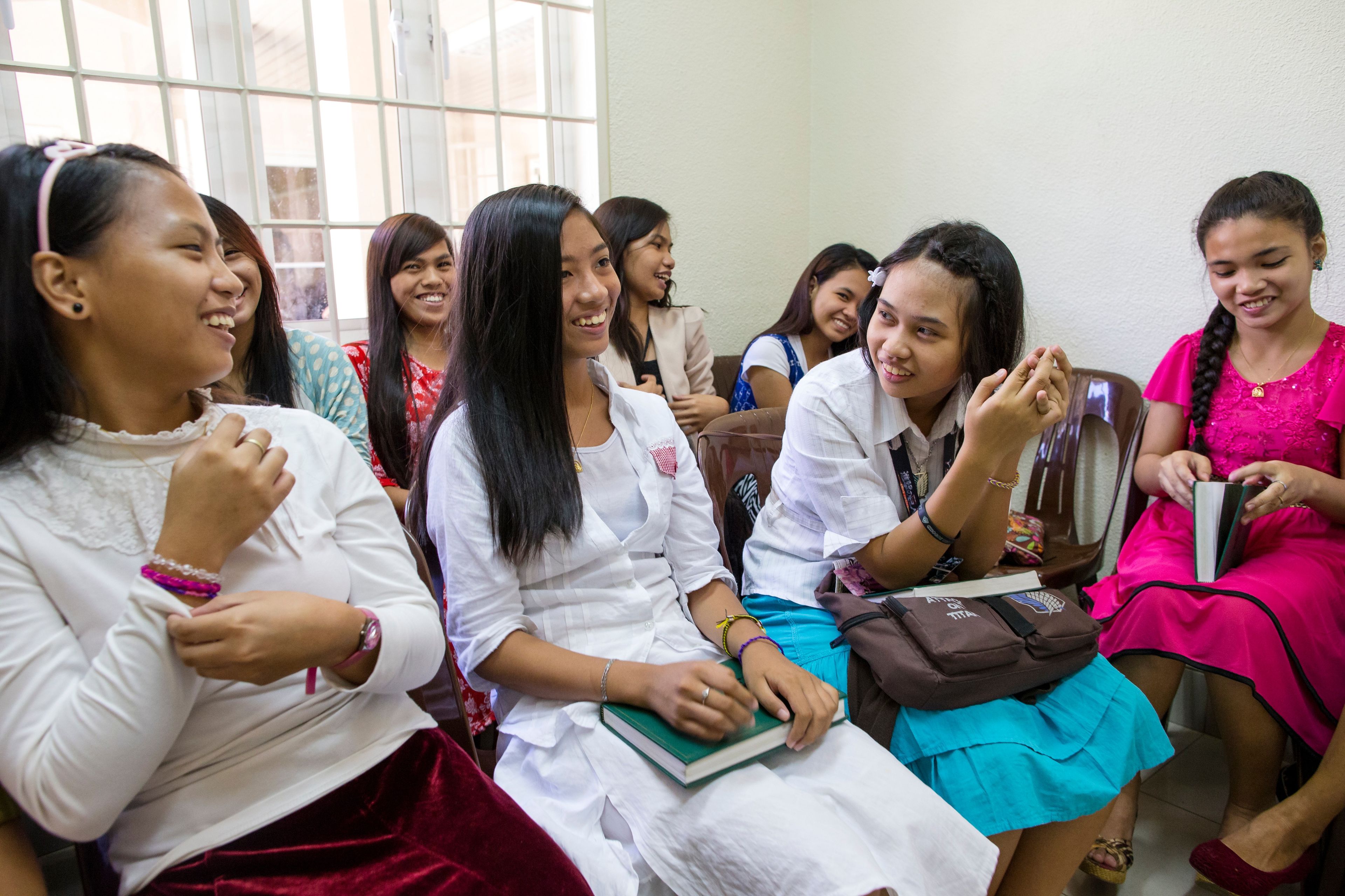 A group of young women in the Philippines sitting in a class with scriptures and hymnbooks on their laps.  