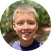 A young boy in a captain america t-shirt smiles while hiking outside.