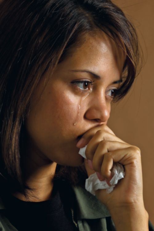 An Hispanic young woman crying.  She is holding a handkerchief.  Tears are rolling down her face.