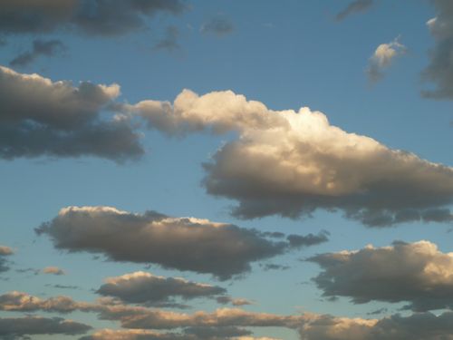 Small groups of white and gray clouds are spread out over a big blue sky.