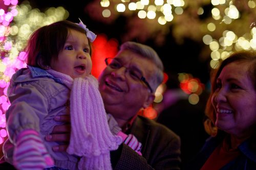 An elderly couple carrying their infant granddaughter, who looks in awe at the Christmas lights on Temple Square.
