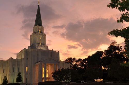 The Houston Texas Temple in the evening, just after sunset, with a purple and pink sky in the background and the shadows of trees over to the right side.
