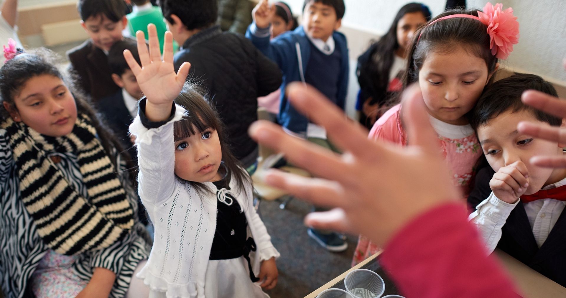 A little girl raising her hand among other small children.