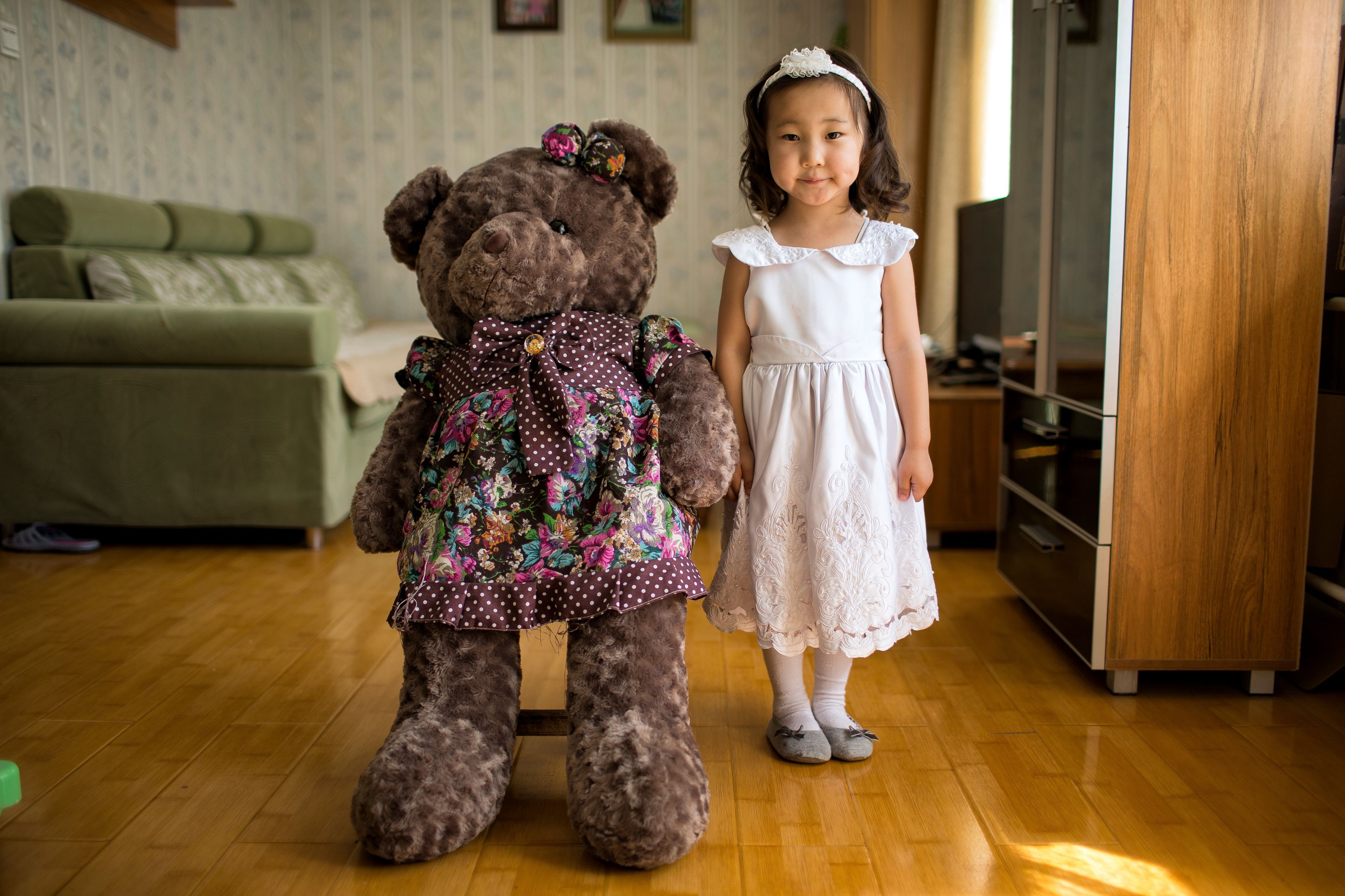 A young Mongolian girl with a white dress and a teddy bear.  
