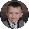 A young boy about 5 years old is dressed in suit and tie (no jacket, just vest).  He's sitting on a wood floor for his portrait.