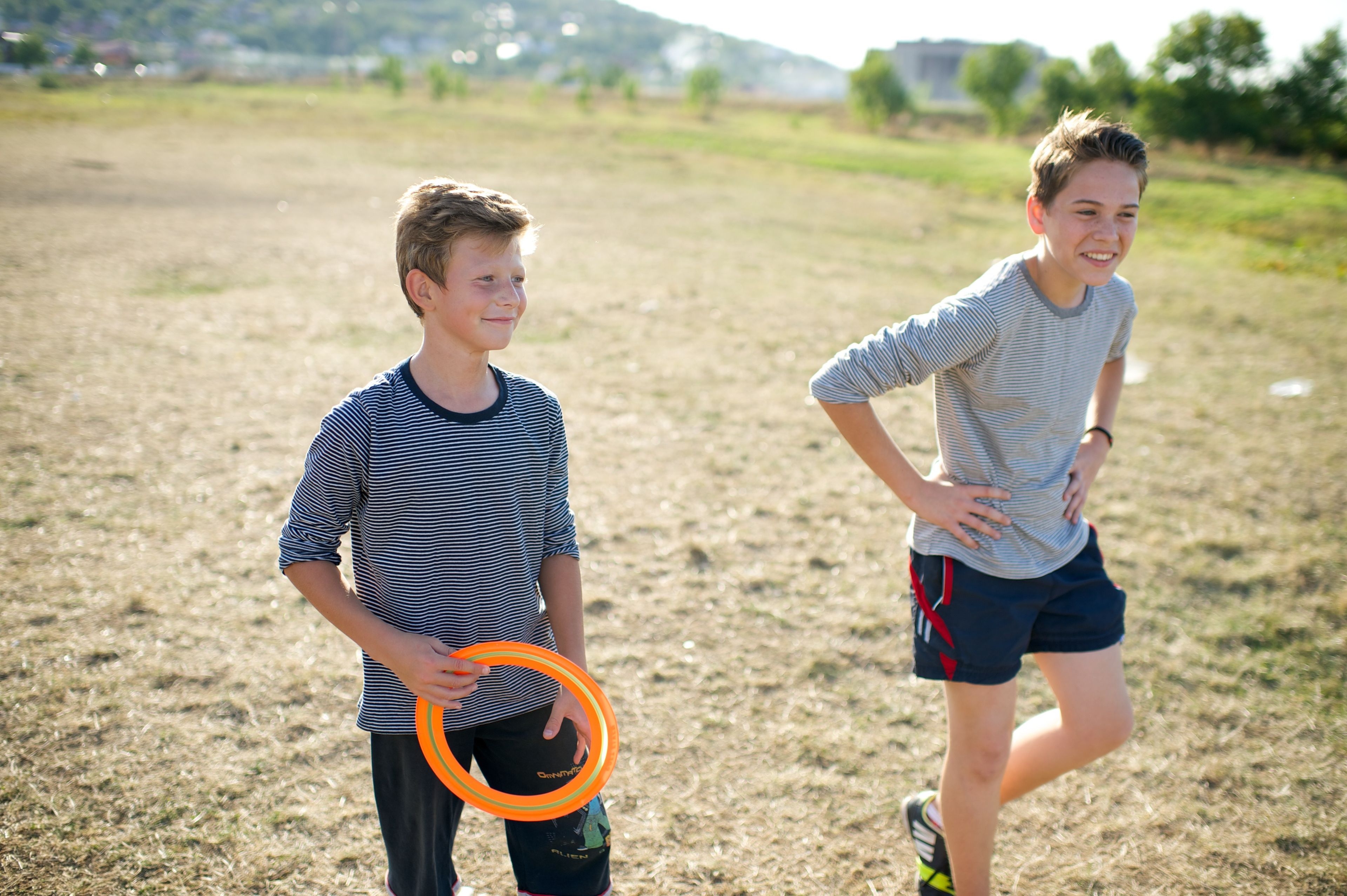 A young man stands holding a Frisbee next to another boy.