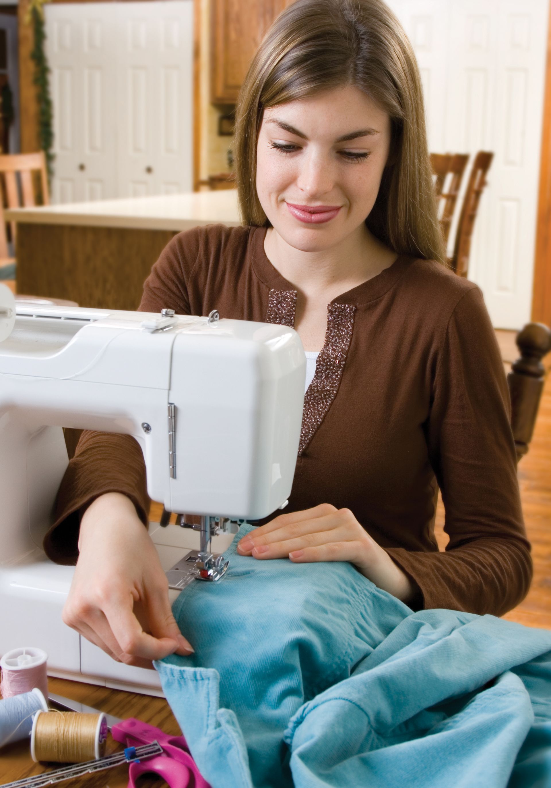 A young woman sits at a sewing machine and sews clothing.