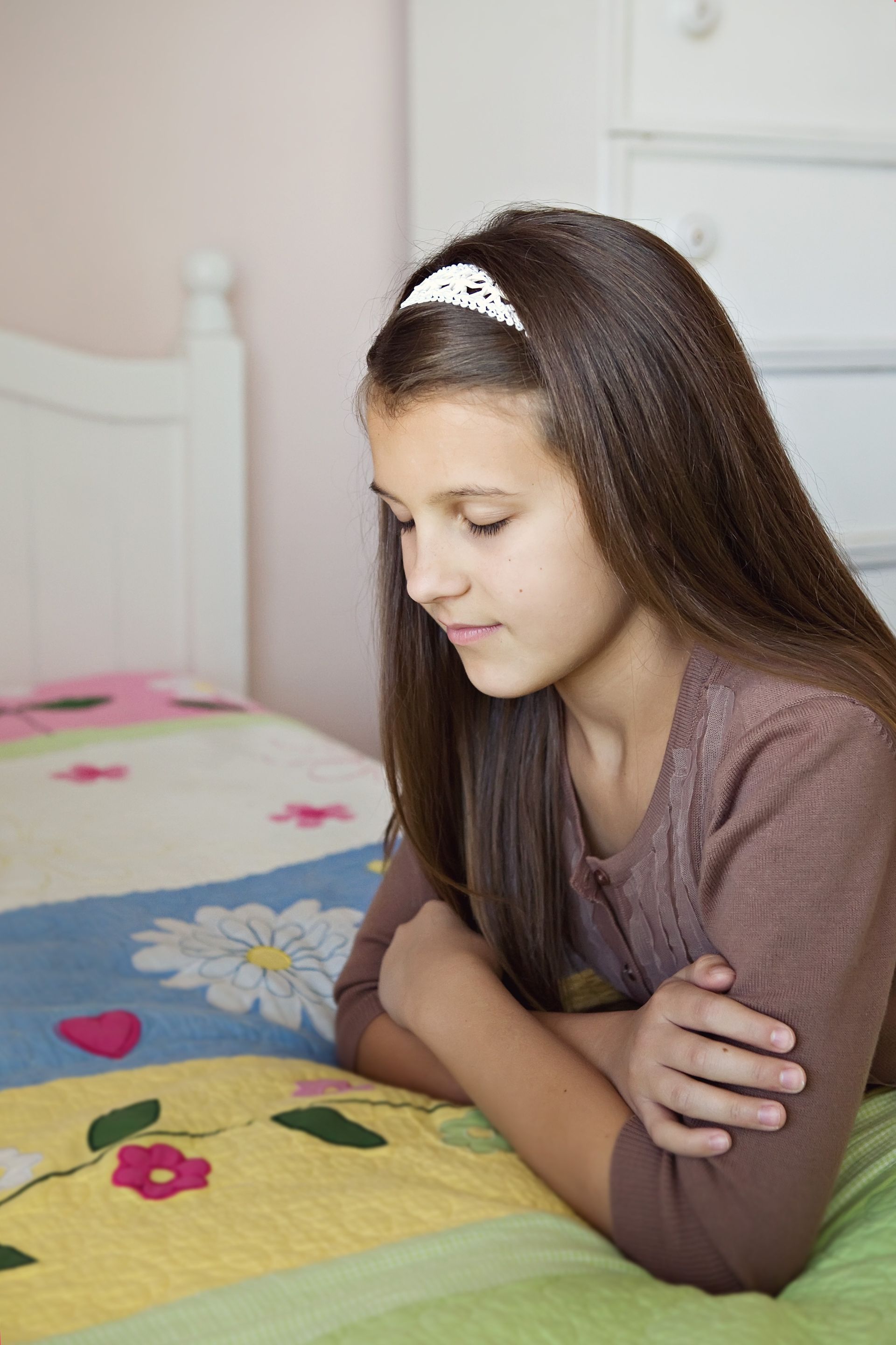 A young girl kneels in her bedroom and prays.