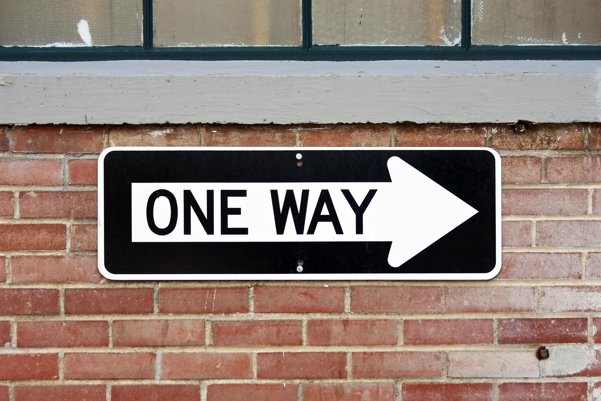 A one-way sign mounted on a red brick wall.