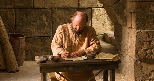 Imagen de un hombre en un escritorio escribiendo en pergamino
