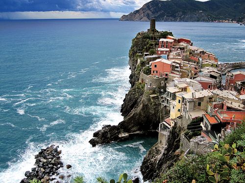 A small village on a cliff against the sea in Italy with storm clouds in the distance.