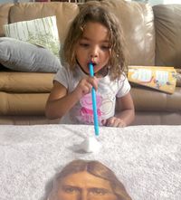 girl blowing cottonball with straw