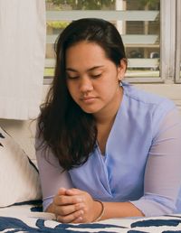 A young Polynesian woman kneeling in prayer beside her bed.