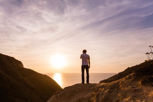 young adult man standing atop a mountain