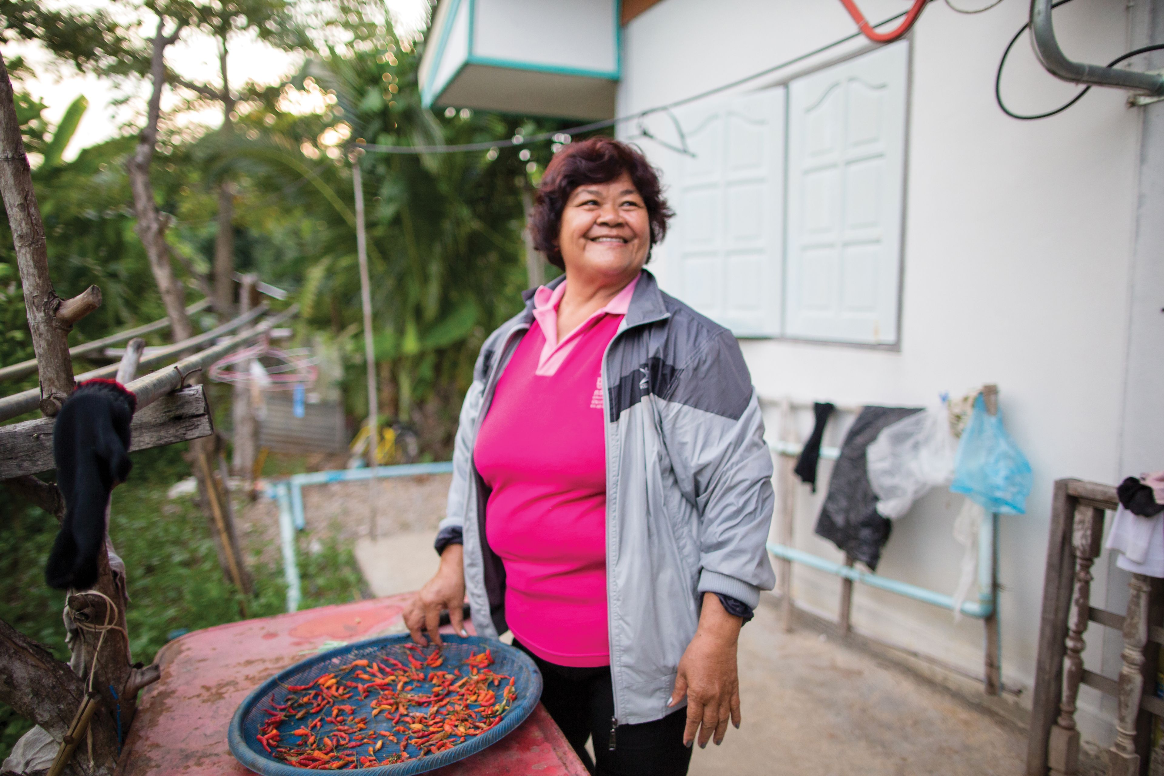 A woman stands outside in Thailand, drying chilies on a platter.