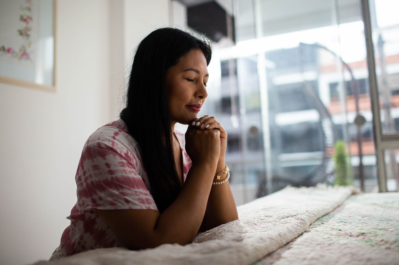Una mujer rezando junto a su cama