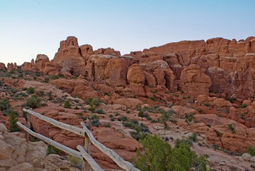 A wooden fence surrounded by rocks and green brush on a trail in Moab.