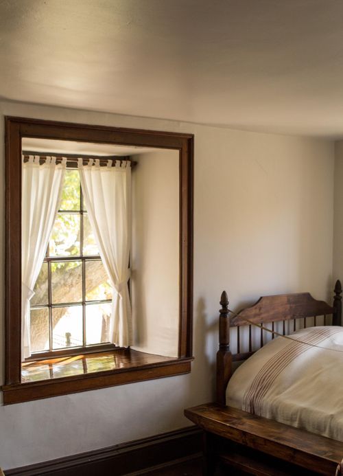 A bed sits next to a window with white curtains in a bedroom of Carthage Jail.