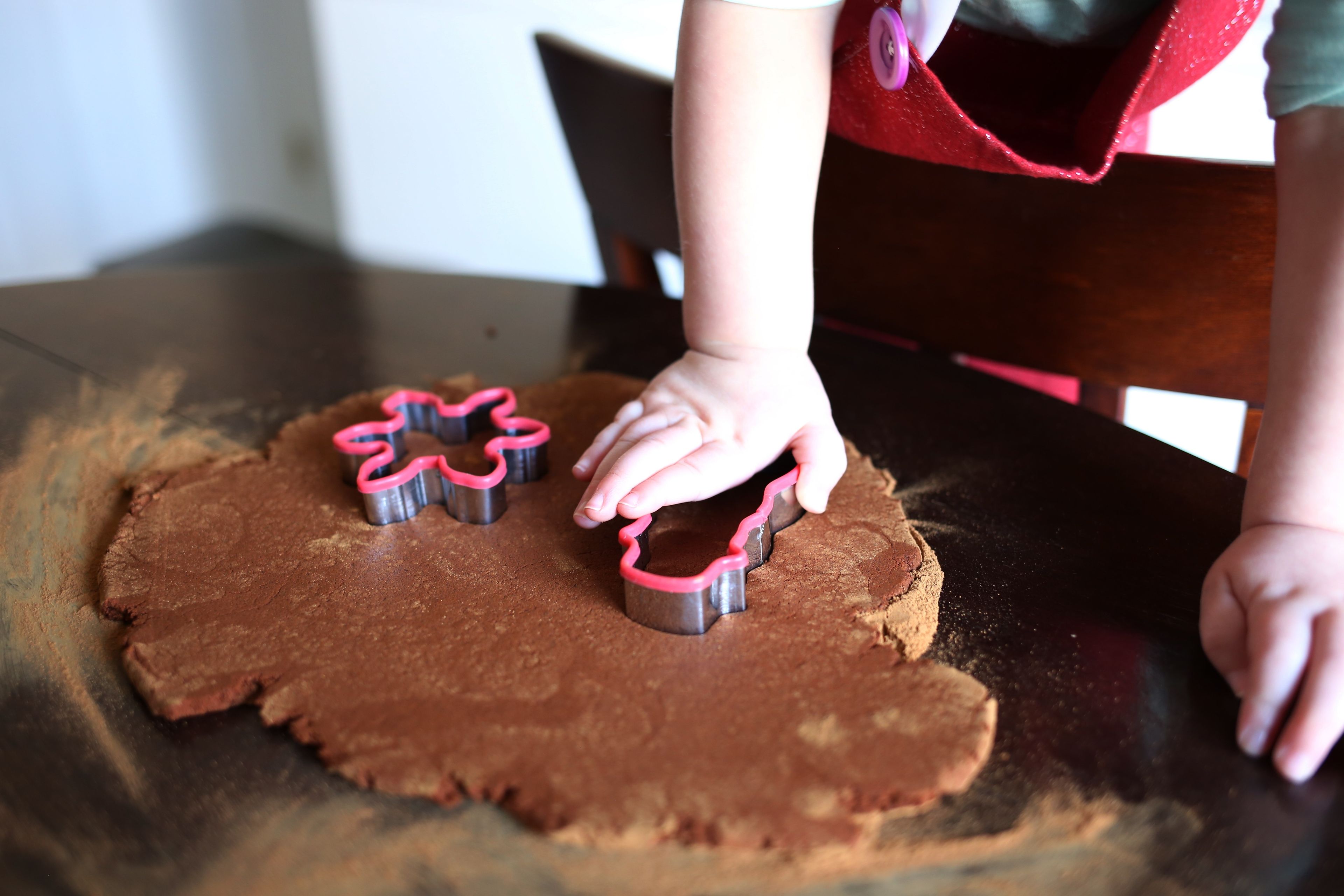 A young child using cookie cutters to cut out Christmas cookies.