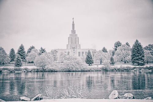 The Idaho Falls Idaho Temple and snow-covered trees reflected in the icy river.
