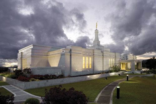 A view of the side of the Suva Fiji Temple, including the path through the grounds leading to the entrance, with the temple lit up in late evening.