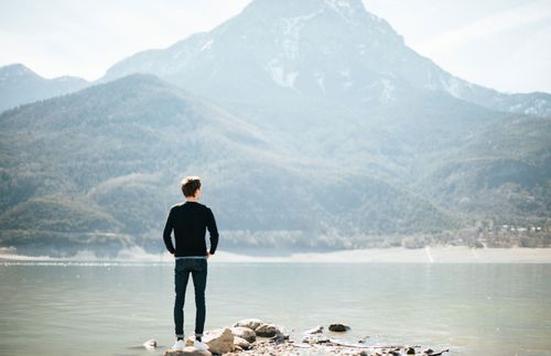 young adult man standing on shore of lake