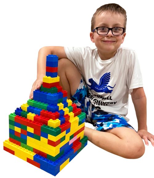 A young boy sits with a stack of Legos. It appears to be a temple he has created.