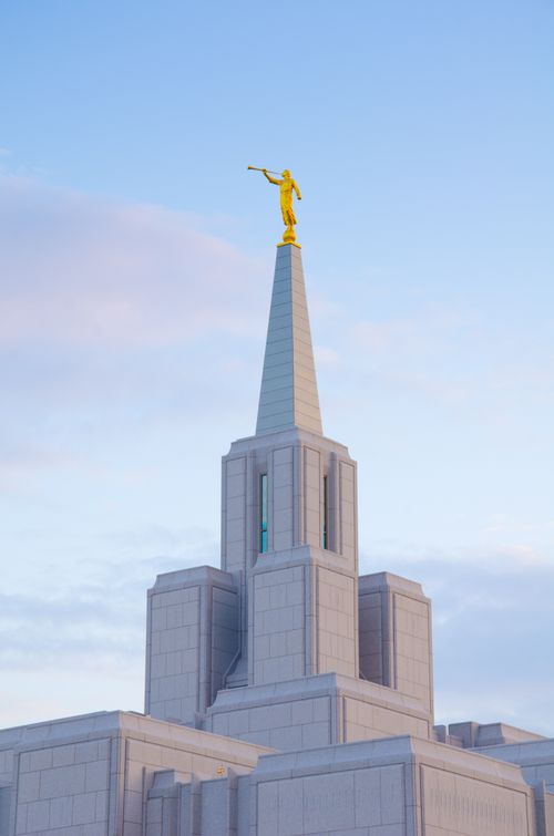 The spire and angel Moroni on top of the Calgary Alberta Temple, with a light blue sky in the background.