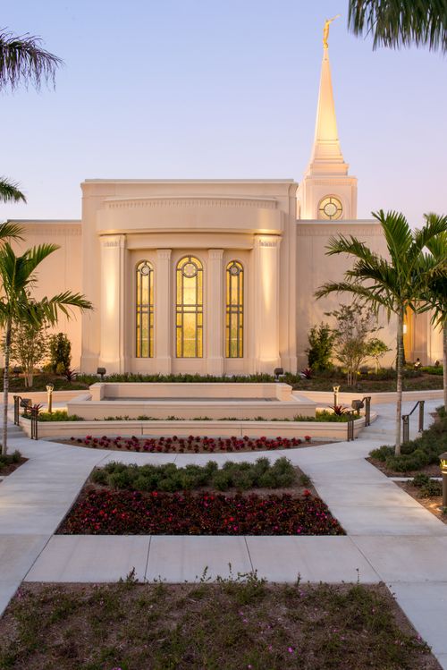 A side view of the Fort Lauderdale Florida Temple in the evening, showing a large stained-glass window with yellow light coming through.