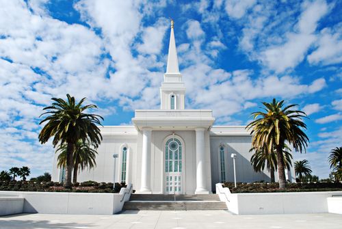 The front of the Orlando Florida Temple, with a vibrant blue sky and fluffy white clouds above and palm trees growing on either side of the temple.