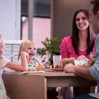 Parents and two young girls sitting at a table eating dinner.