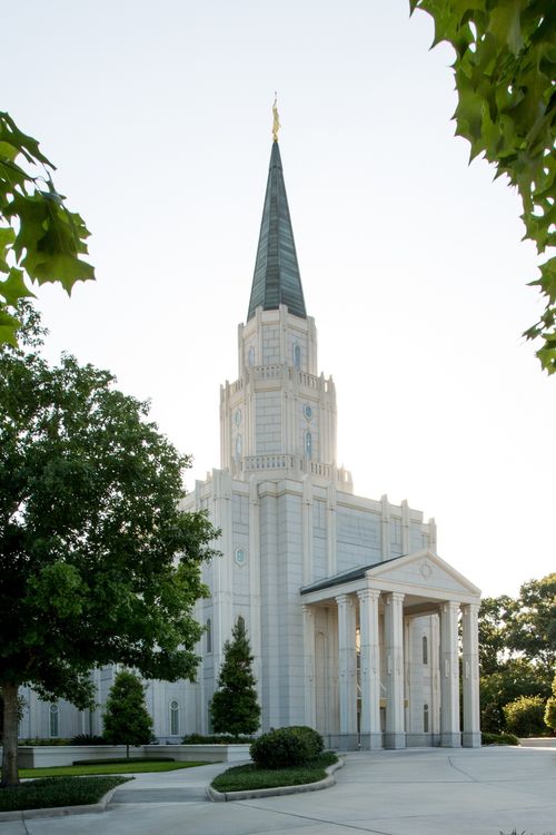 A portrait of the Houston Texas Temple, framed by green leaves on nearby trees, during the daytime.