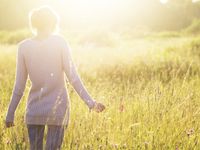 A young woman wandering through a grassy meadow, as sunshine falls on her. (horiz)