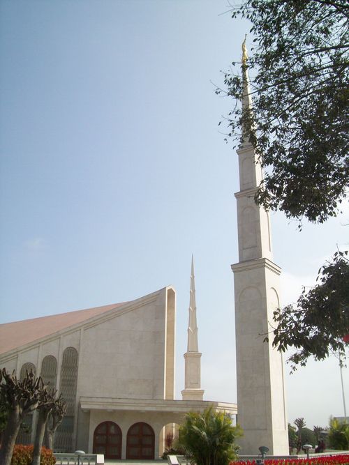 The main spire of the Lima Peru Temple, partially covered by a large green tree and with part of the front of the temple showing on the left side.