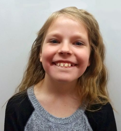 A portrait of a young girl about 8 smiling. Wearing a gray and black shirt.