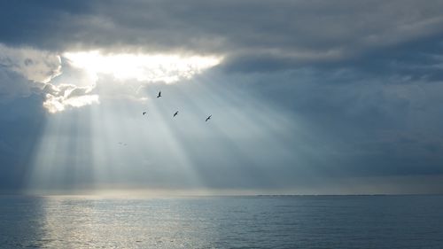 A thick layer of gray clouds spread out over the ocean, with sun rays breaking through a hole in the clouds.