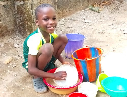 Boy washing dishes with buckets of water