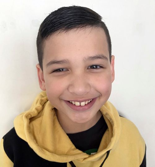 A young boy stands for a portrait. He is wearing a brown hoodie