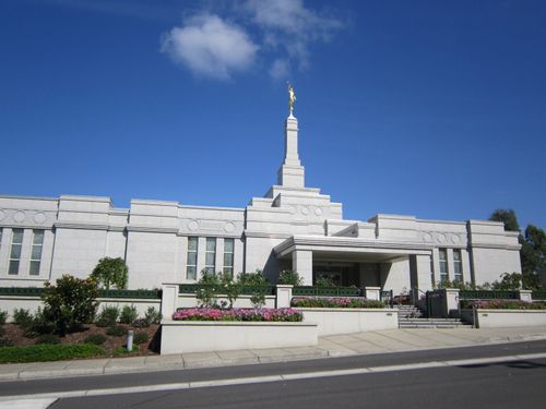 A view of the Melbourne Australia Temple exterior entrance and grounds with flowers, seen from across the street on a sunny day.