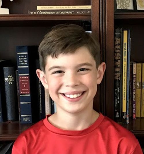 A young boy named Jack stands for a photo in front of a bookshelf